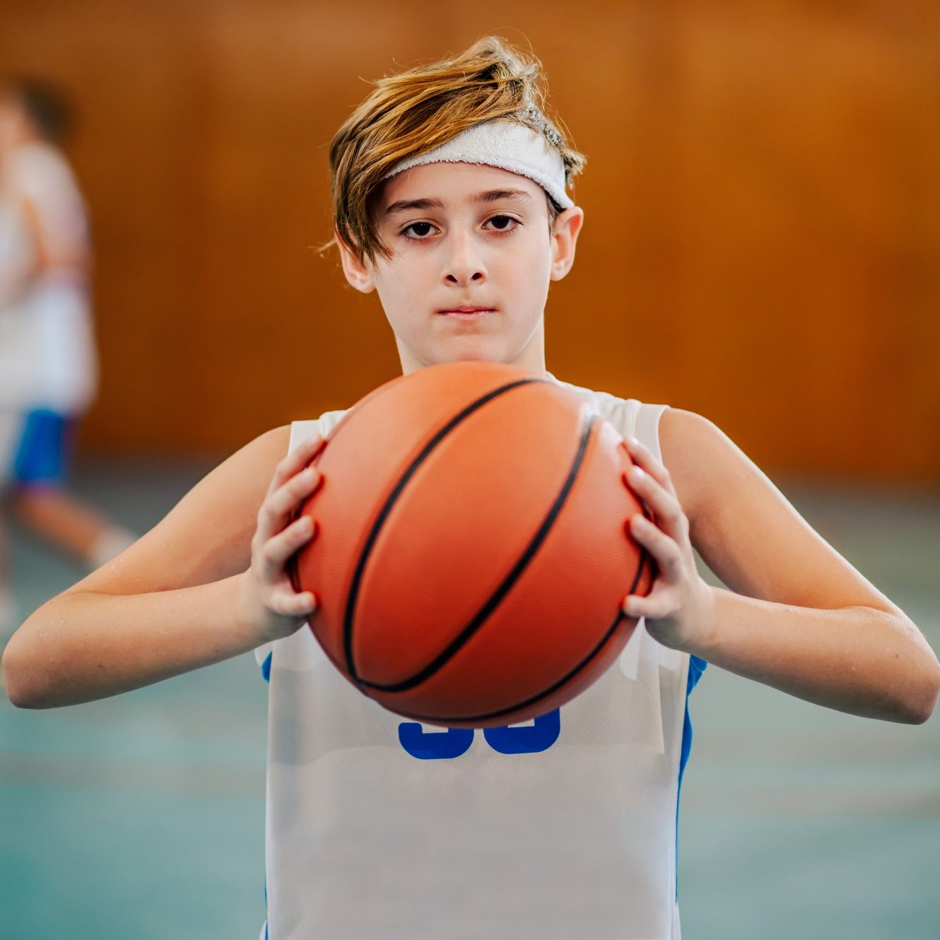 A junior basketball player is holding a ball on court during training.